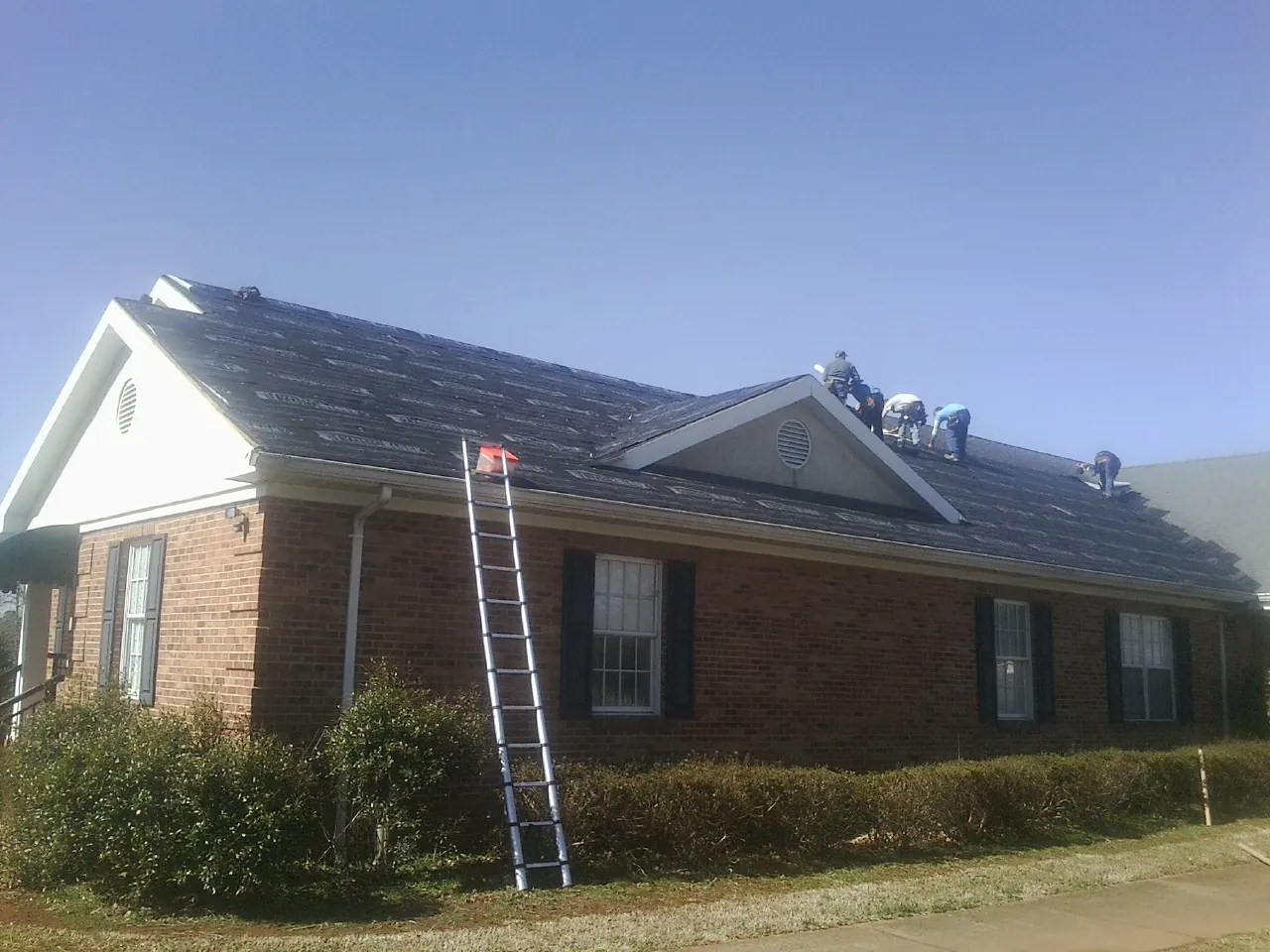 Crew tearing shingles off a brick ranch roof with a ladder set — Emergency Roof Repair work by our crew in Chatsworth